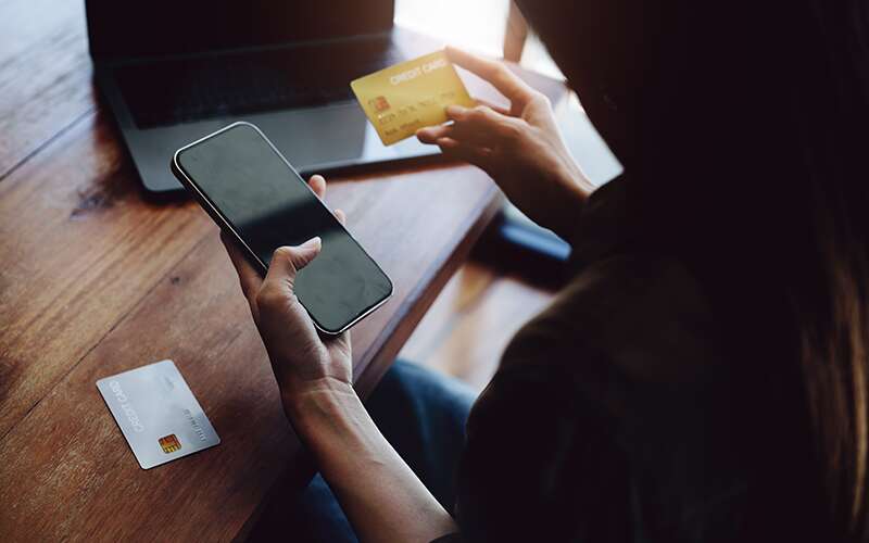 Woman looking at her phone while holding a credit card representing an E-commerce transaction.