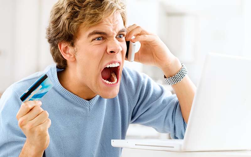 A customer angrily holds his credit card while on the phone.